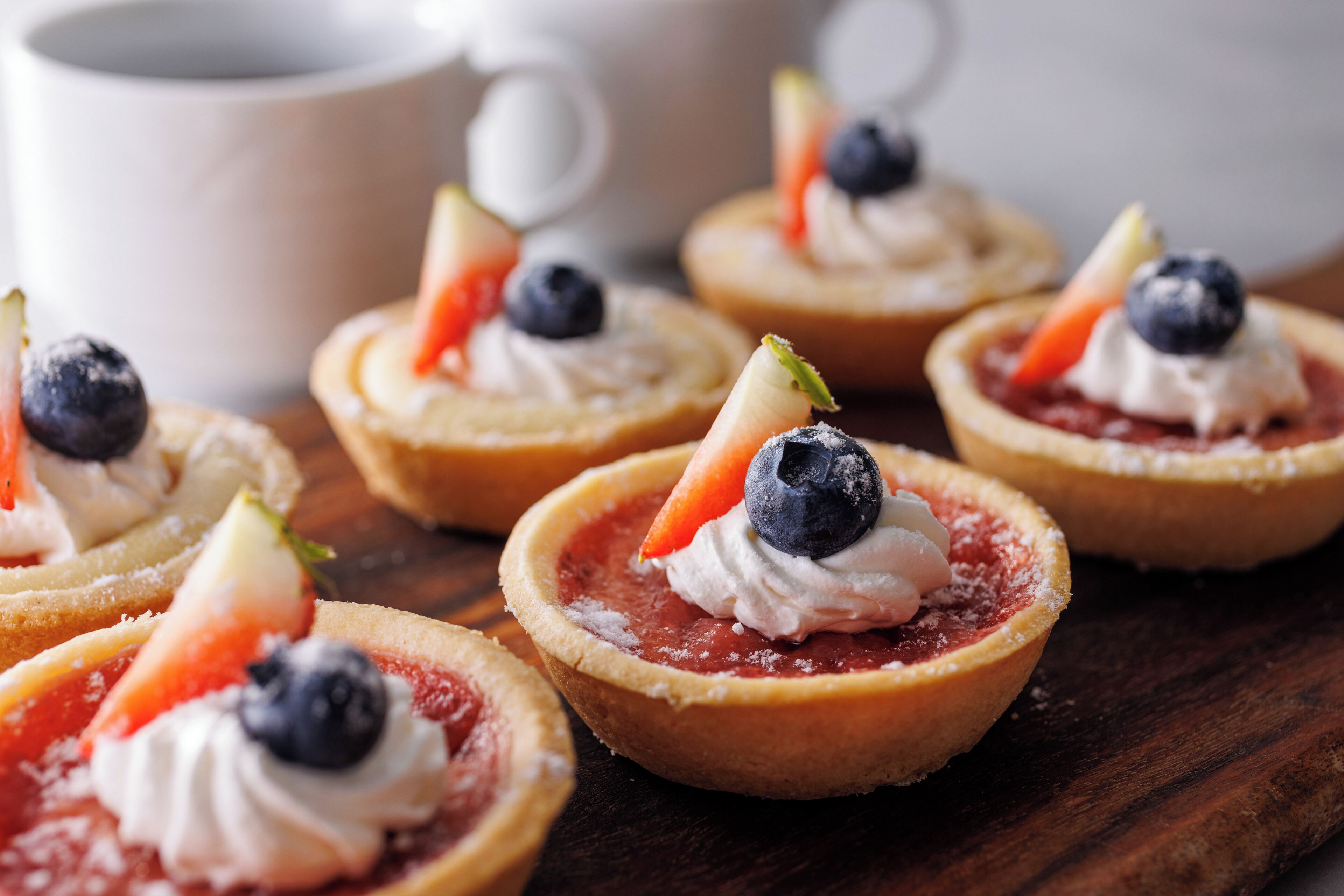 Una selección de tartaletas de frutas con crema batida y frutos rojos sobre una tabla de madera.