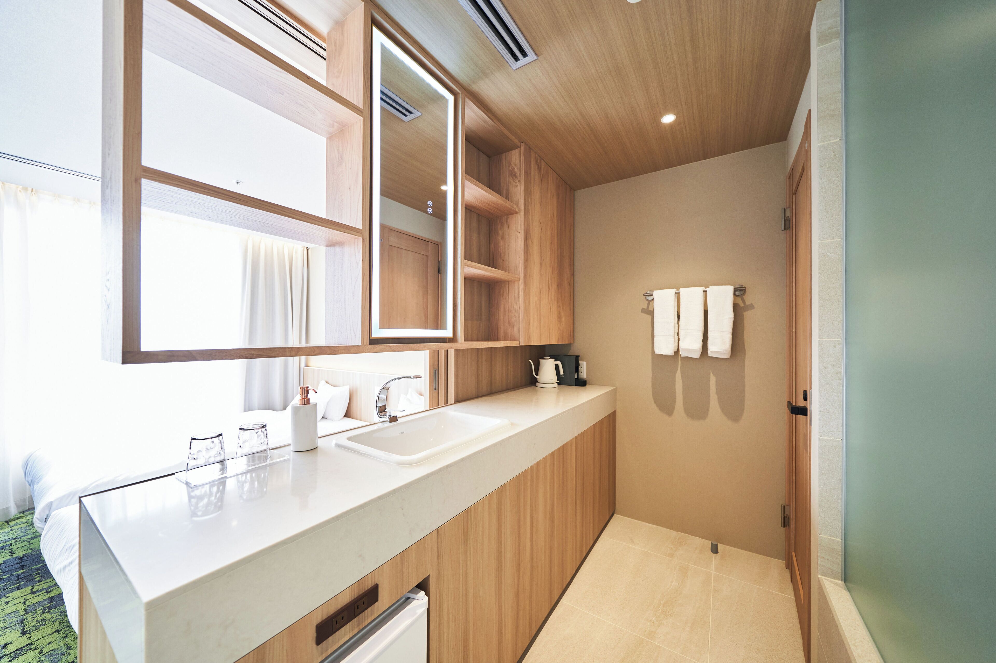 A modern bathroom with a large mirror, wooden cabinets, a sink, and a shower area.