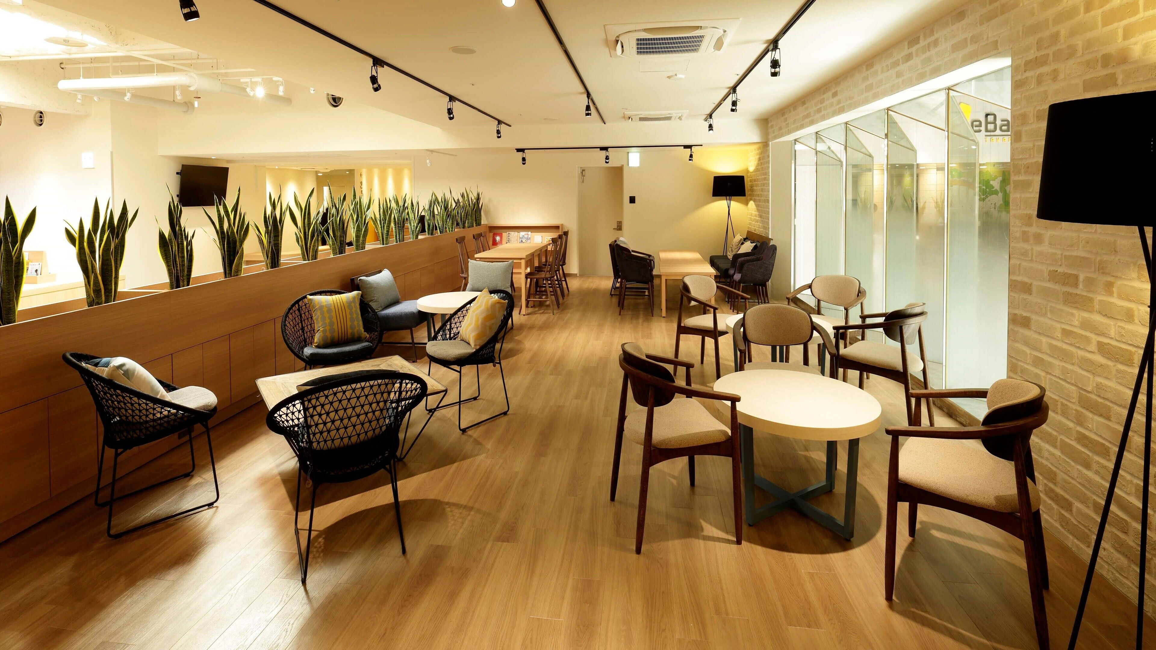 Un interior moderno con suelo de madera, sillas de madera y color negro, una partición de vidrio y plantas en macetas.