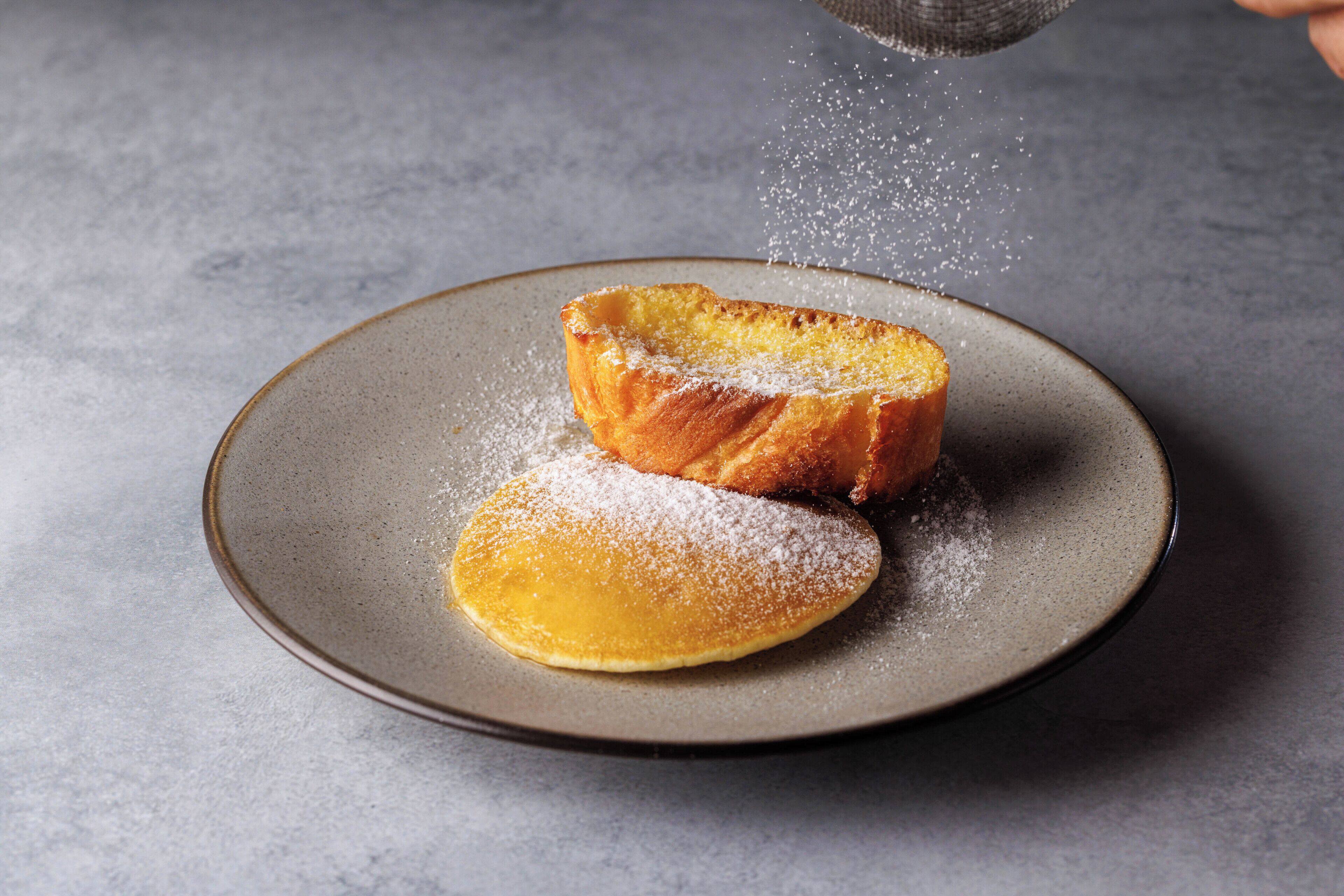 A plate with a piece of bread and a pancake dusted with powdered sugar.