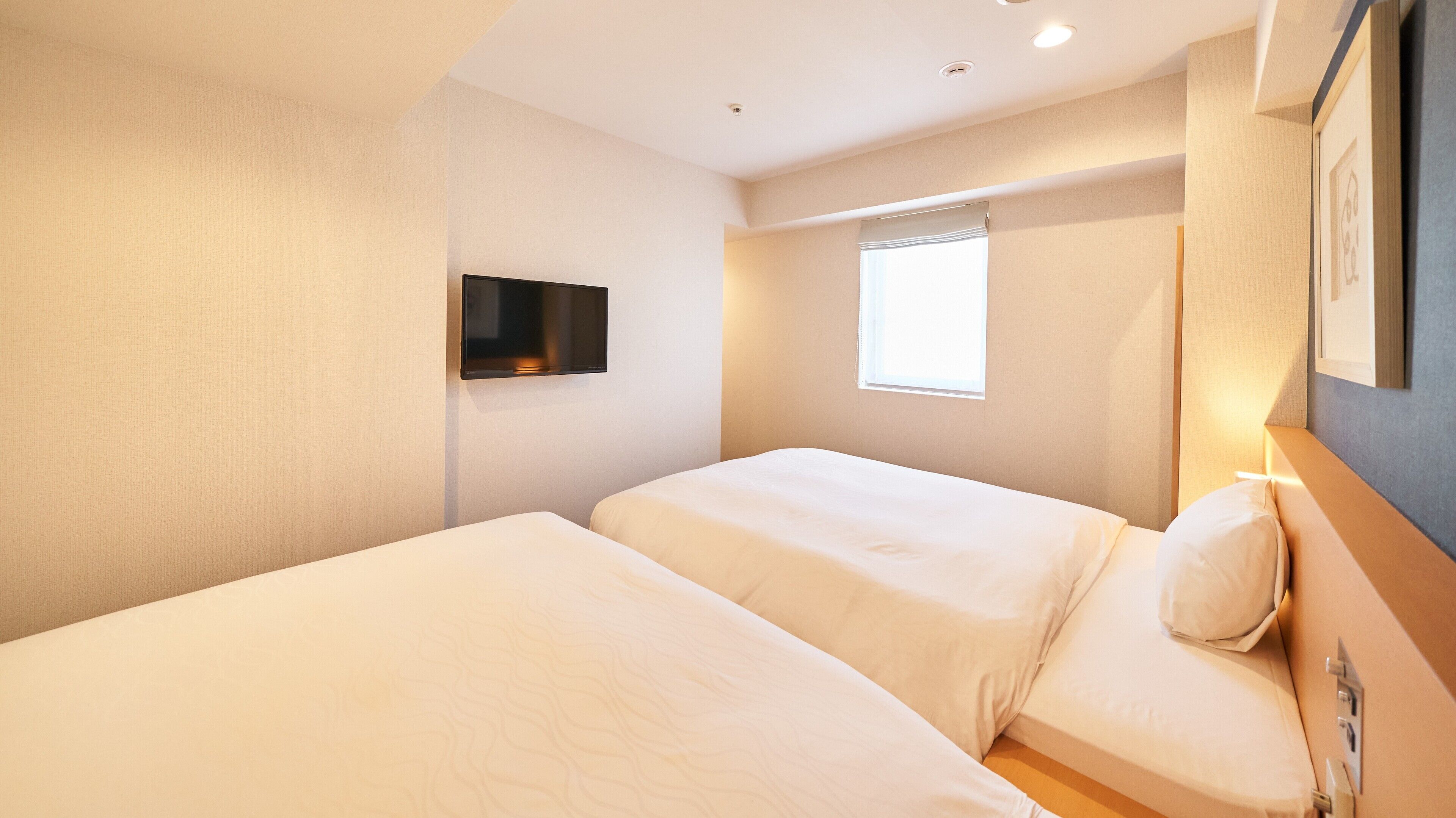 A hotel room with two beds, a flat-screen TV mounted on the wall, and a window with curtains.