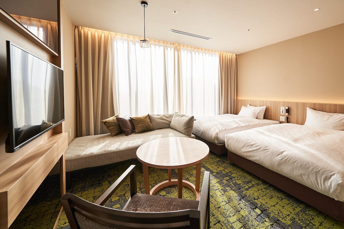 A hotel room with two beds, a sofa, a TV, and a small table.