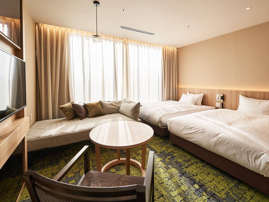 A hotel room with two beds, a sofa, a TV, and a small table.