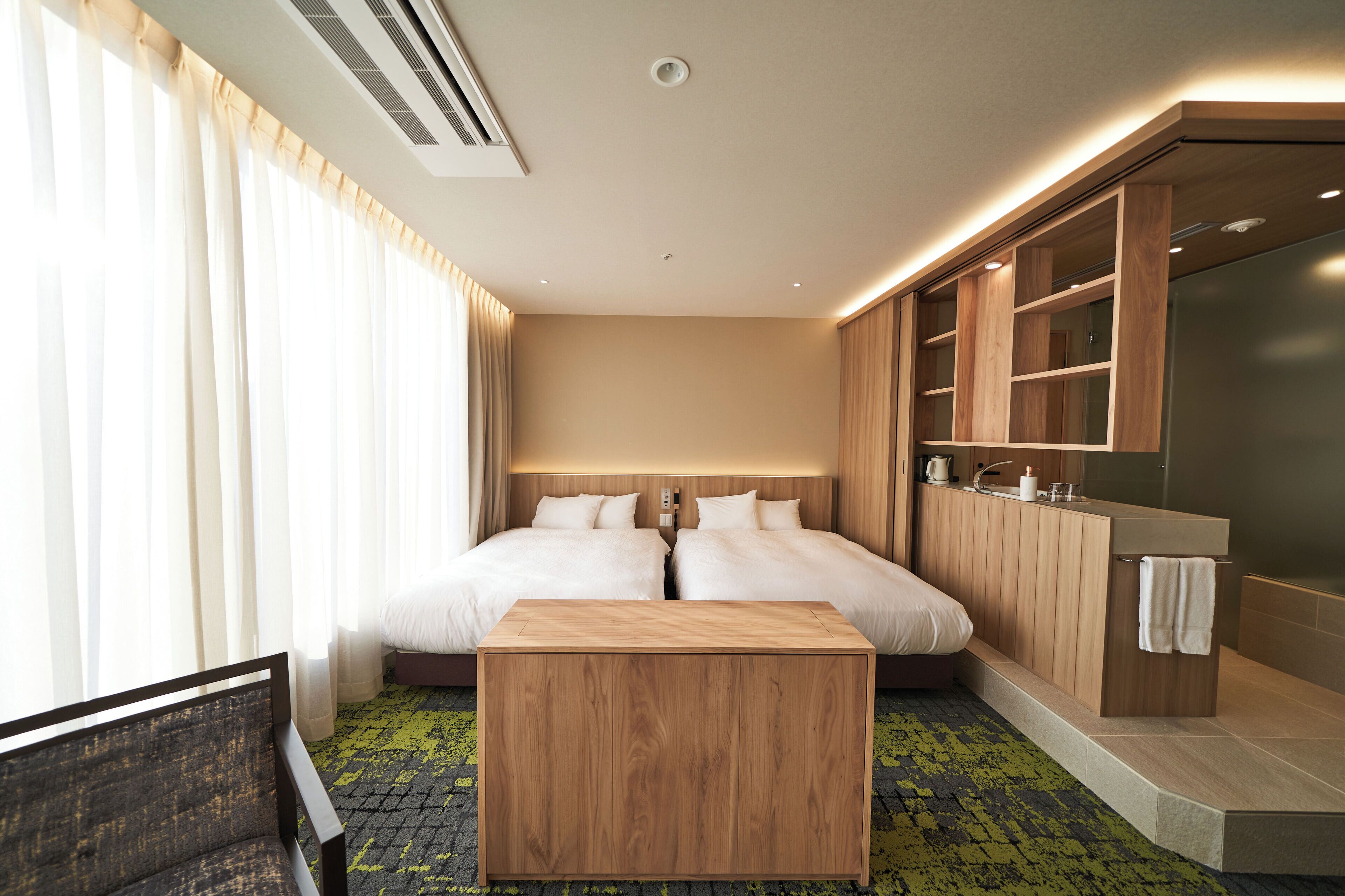 Habitación de hotel con cama doble, mesita de noche de madera, armario empotrado y un amplio ventanal con cortinas.