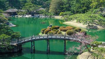 Un giardino tradizionale giapponese con un ponte di legno sopra uno stagno, immerso nel verde e con un piccolo padiglione.