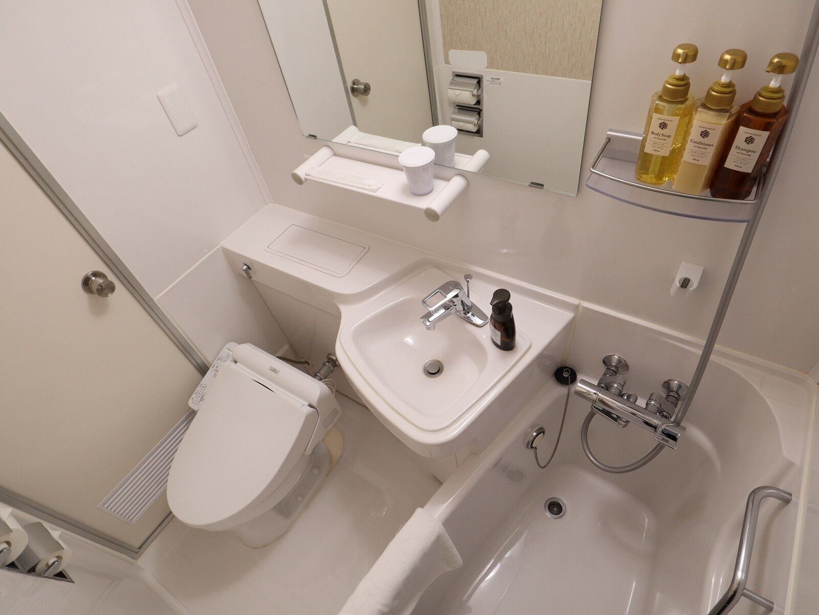 A modern bathroom with a toilet, sink, and bathtub. There are toiletries on a shelf and a mirror above the sink.