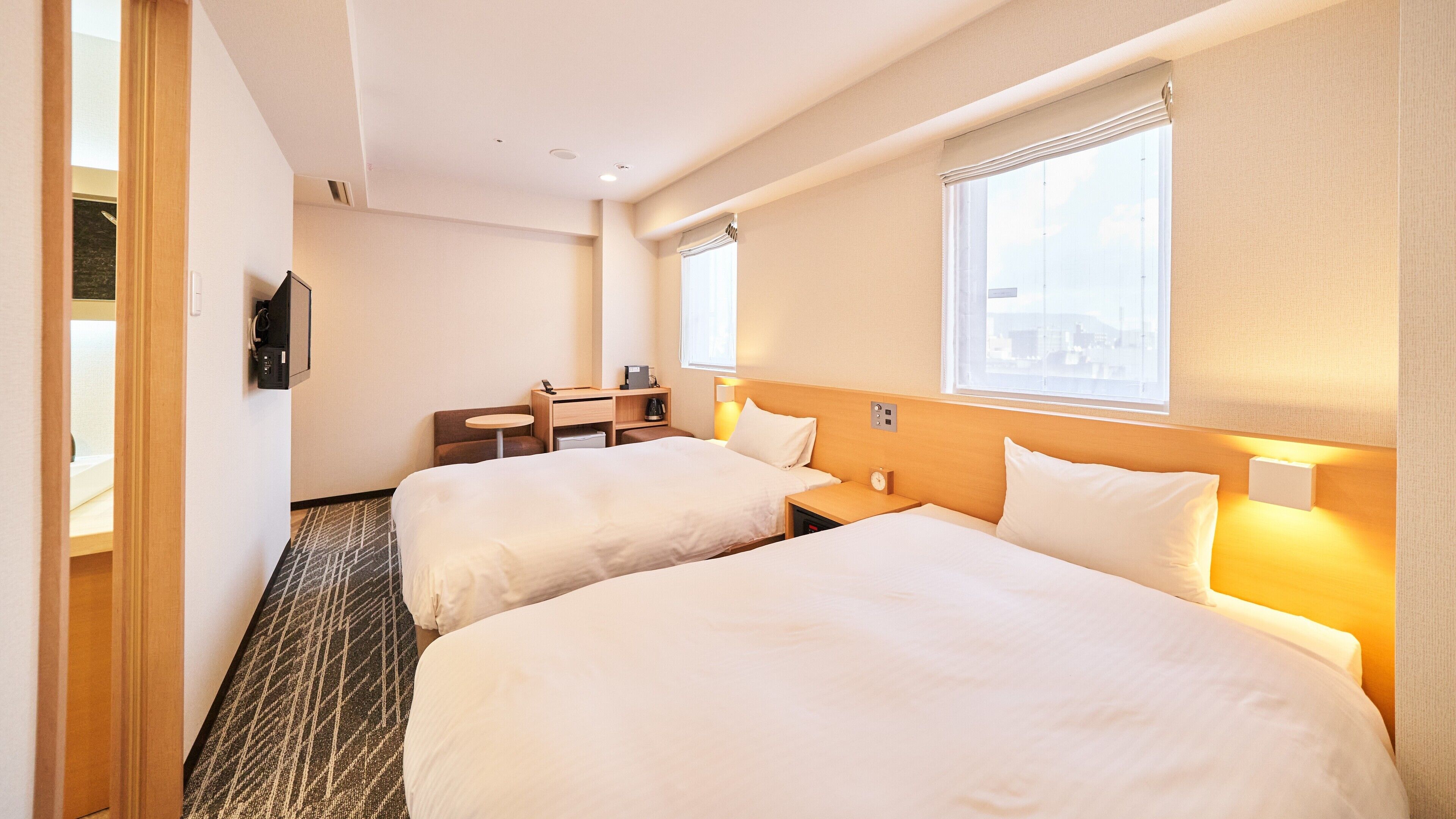 Habitación de hotel con dos camas, un escritorio, una silla, una mesita y una ventana.