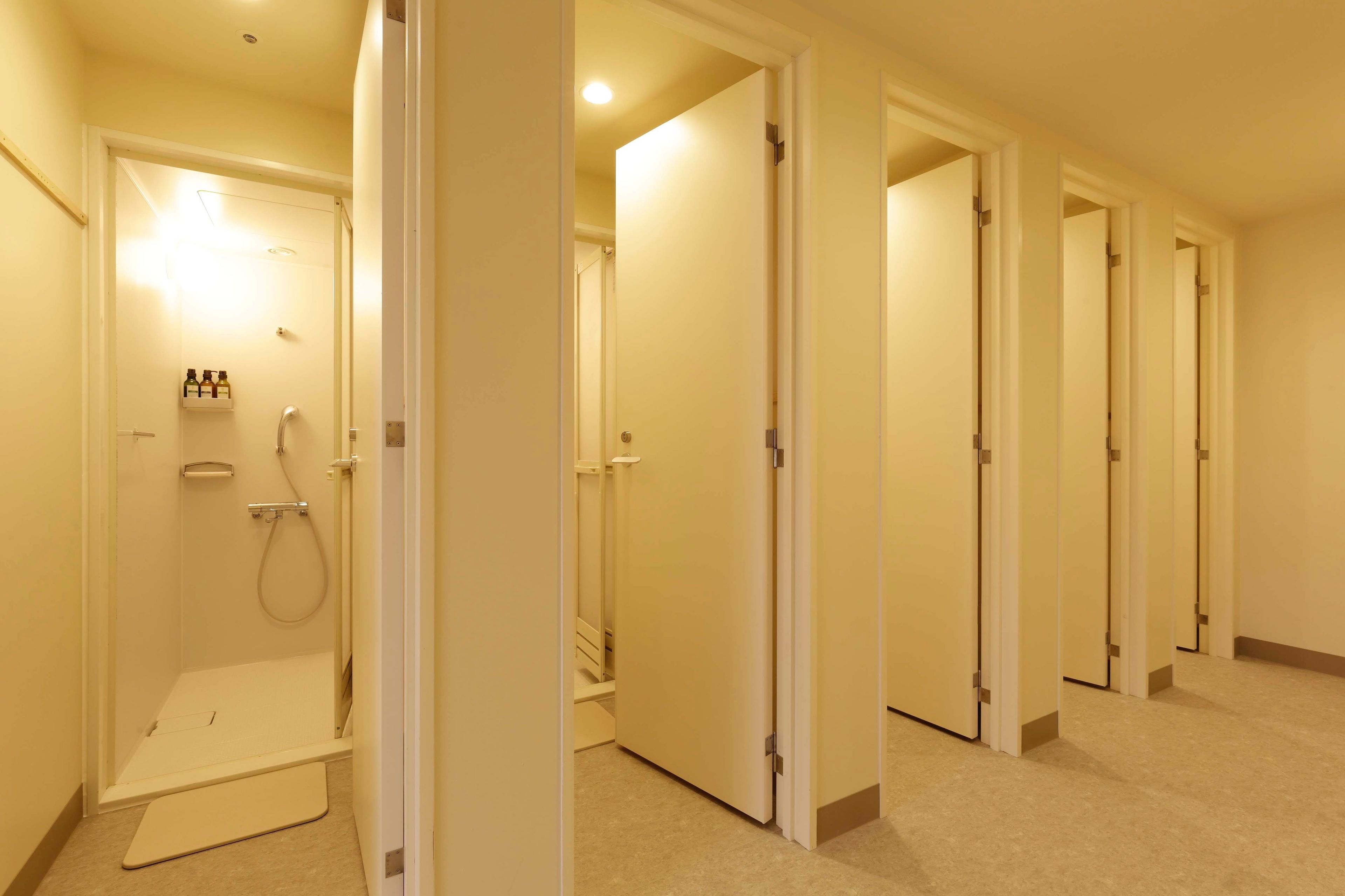 A hotel hallway with multiple doors, a shower area with a glass enclosure, and a small shelf with bottles.