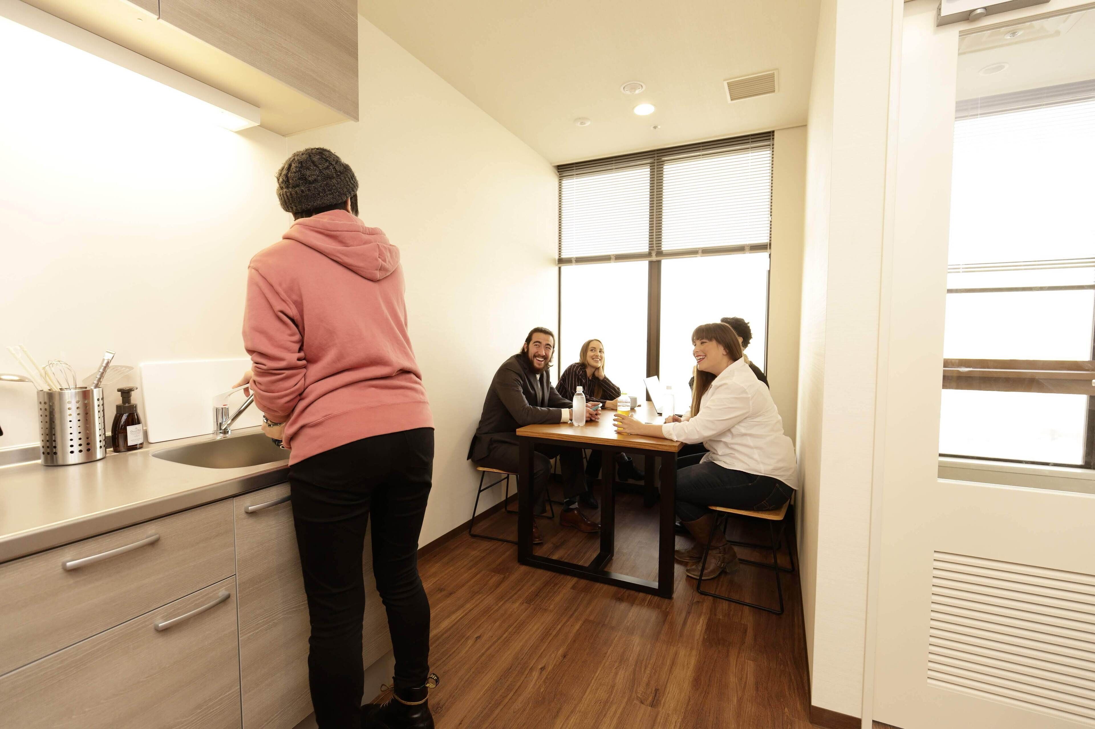 Una cuina moderna amb un rentaplat, taulell i un grup de persones assegudes a la taula.