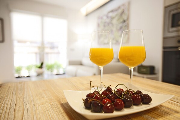 A dining table with two glasses of orange juice and a plate of cherries.