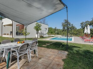 Een zwembadgedeelte met een overdekte patio, een zwembad en ligstoelen.