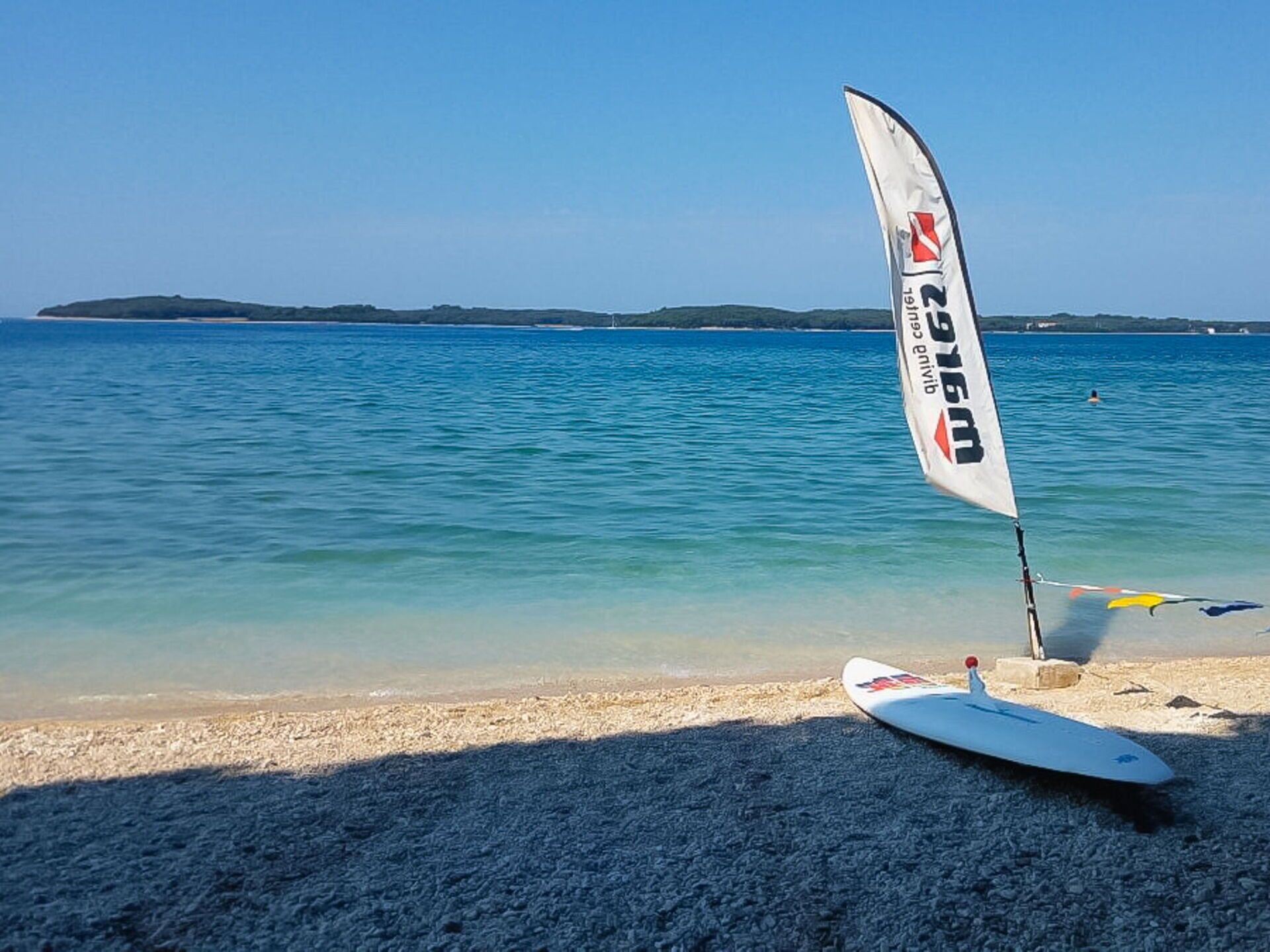 A beach with a white surfboard and a sail on the sand.