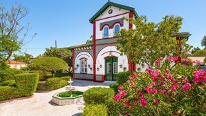 A traditional building with a green door and white walls, surrounded by well-maintained hedges and flowering plants.