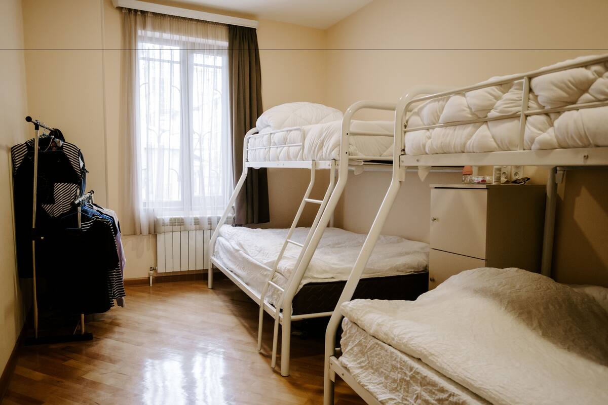 Une chambre de dortoir avec des lits superposés, un radiateur, une fenêtre avec des rideaux et un portant à vêtements.