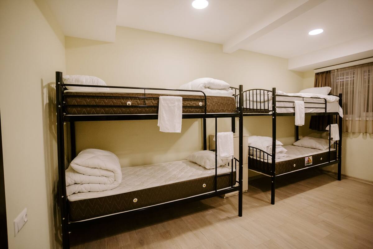 Une chambre avec trois lits superposés, chacun équipé d’un matelas et d’oreillers, ainsi qu’une petite table de chevet avec une lampe.