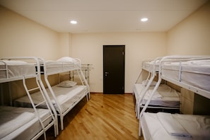 A room with bunk beds arranged in two rows, a wooden floor, and a door in the center. - Viking Hostel (Tbilisi)