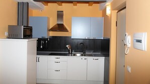 Una cucina compatta con mobili bianchi, un forno a microonde in acciaio inossidabile, uno schienale nero e un soffitto in legno.