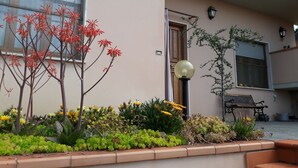 A building with a beige exterior, a wooden door, a black lamp post, and a small garden with various plants and flowers. - Apartment with view of the Tuscan coast and garden (Corsanico)