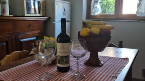 A kitchen with a dining table set for two, a bottle of wine, and a bowl of fruit. - Apartment with view of the Tuscan coast and garden (Corsanico)