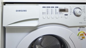 A Samsung washing machine in a kitchen with wooden cabinets above.