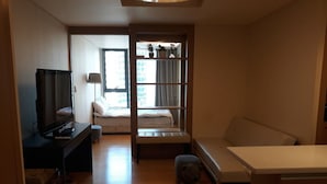 A compact room with a bed, a desk with a computer, a television, a sofa, and a small table.