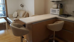 A modern kitchen with a white countertop, a gas stove, a microwave, and two bar stools.