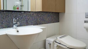 A modern bathroom with a white sink, toilet, and wooden cabinet.