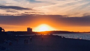 Atardecer sobre una playa con gente y un muelle.