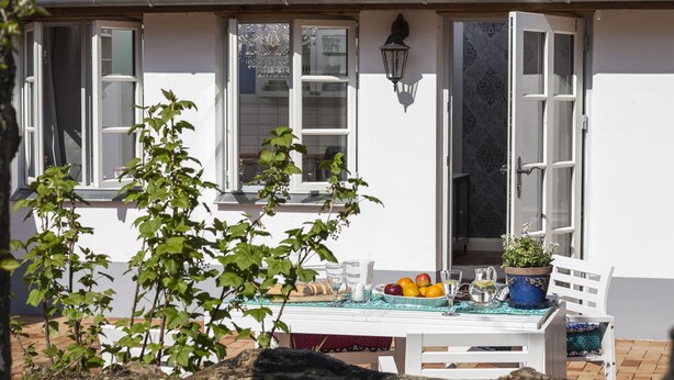 Un patio con mesa lista para comer, rodeado de paredes blancas y ventanas.