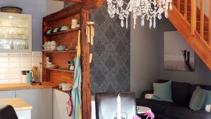 Una sala de estar acogedora con una escalera de madera, una araña, una mesa de comedor con una vela y un sofá con cojines.