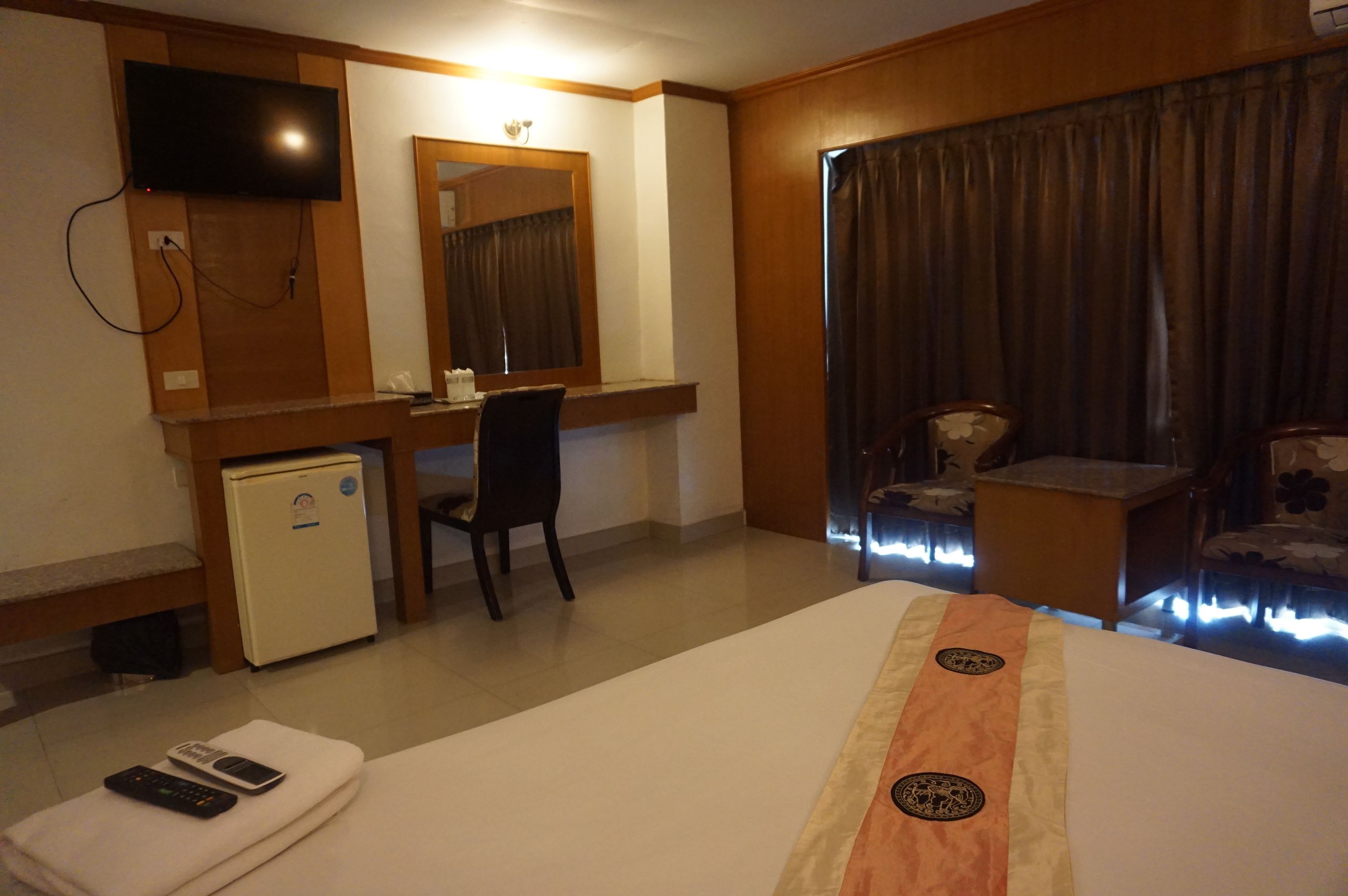 A hotel room with a bed, a desk, a television, a mini-fridge, and a window with curtains.