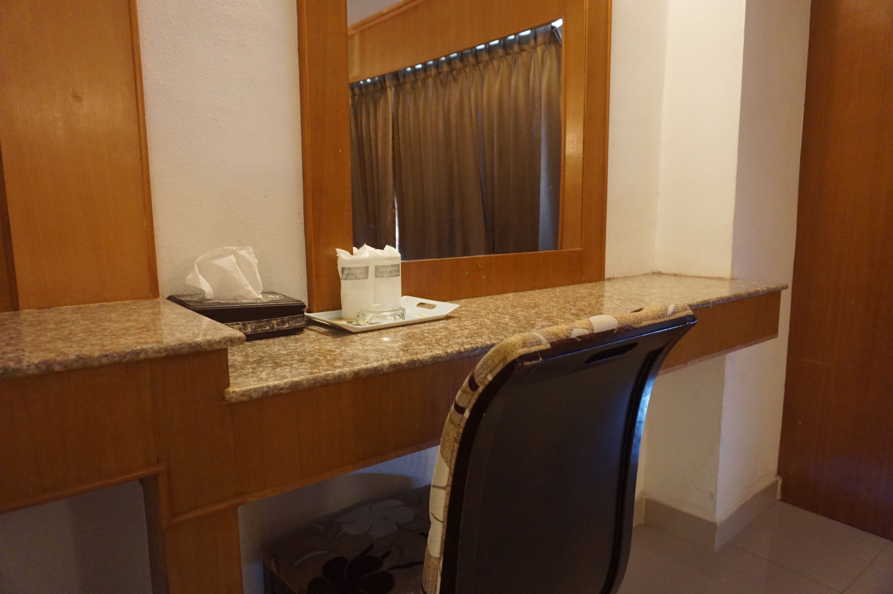 A hotel room with a wooden desk, a chair, a mirror, and a window with curtains.