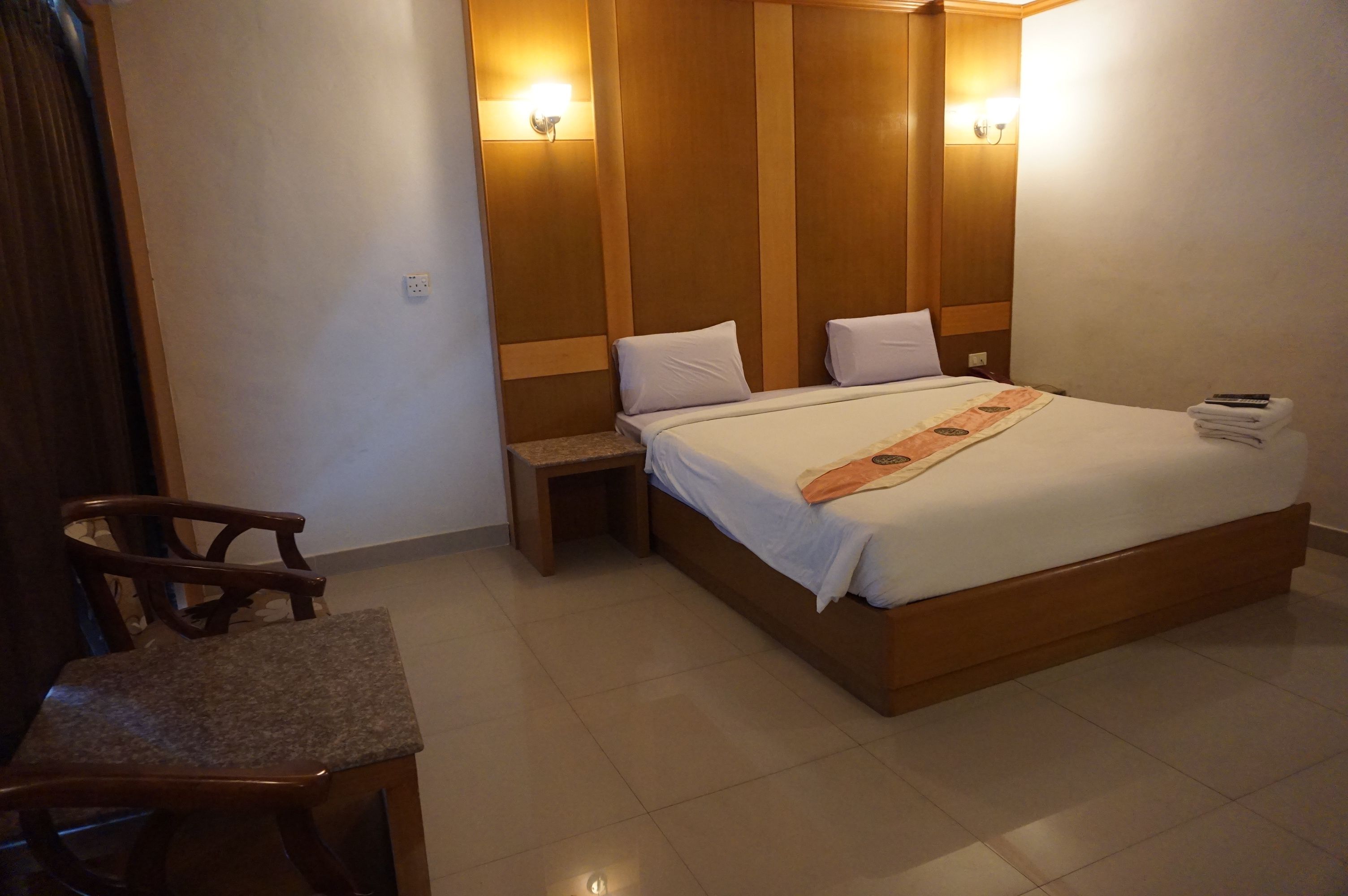 Habitación de hotel con una cama grande, dos mesitas de noche, una silla y un escritorio pequeño.