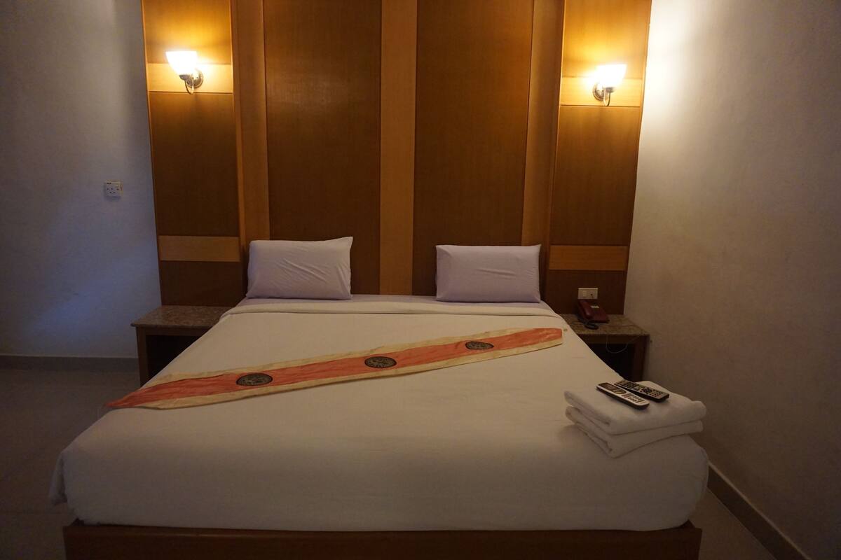 A hotel room with a large bed, two bedside tables, and two wall-mounted lamps.