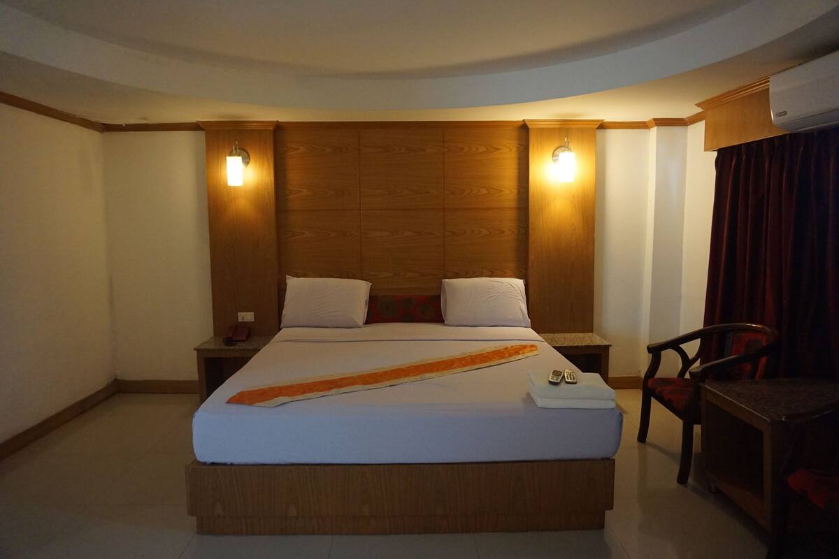 A hotel room with a large bed, two bedside tables, a chair, and a desk.