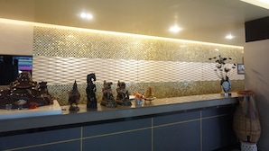 A reception desk with a decorative tiled wall, a vase with flowers, and various small statues. - PP Hotel Dannok (Sadao)