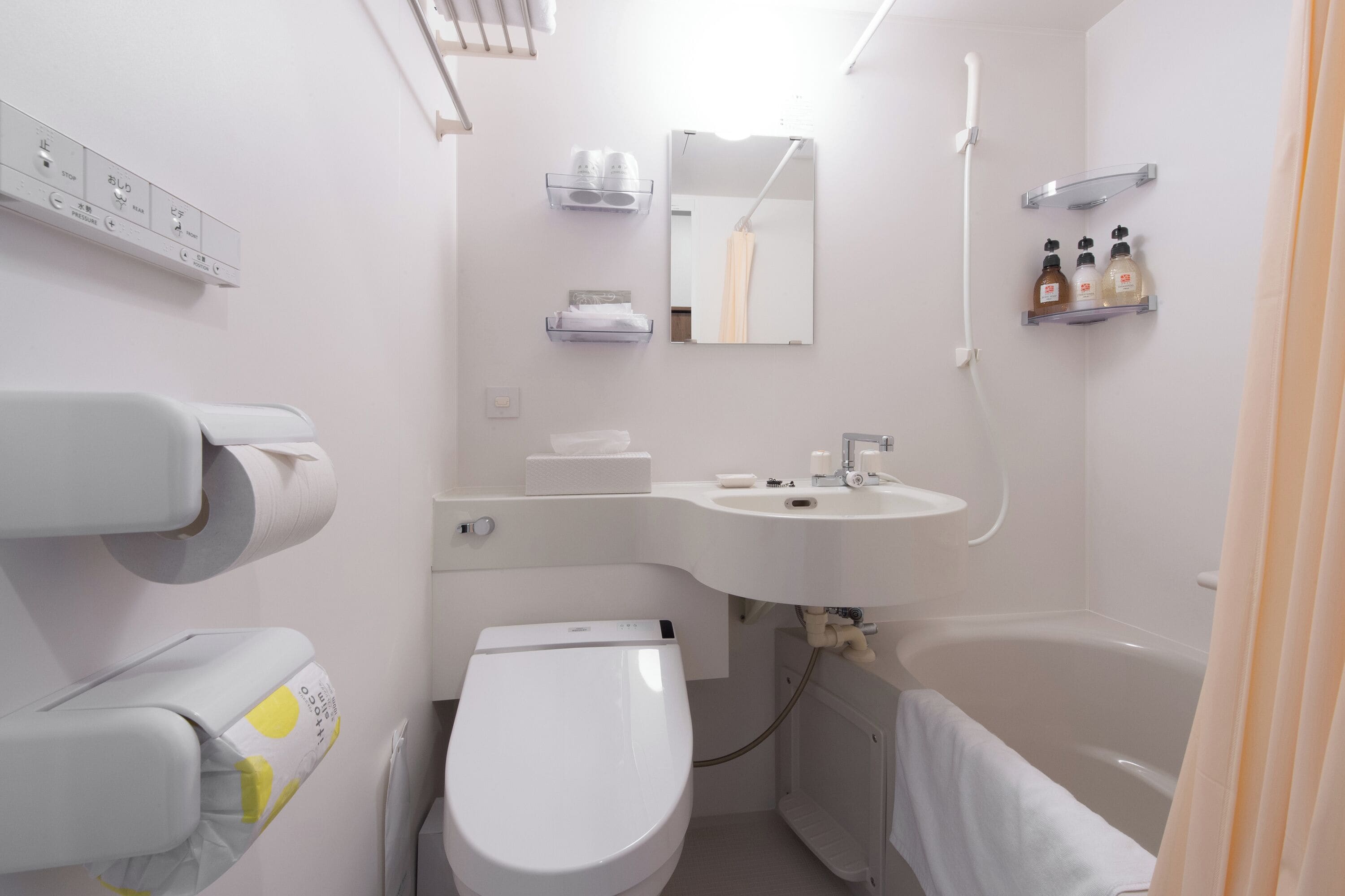 Une salle de bain moderne équipée de toilettes, d’un lavabo et d’une baignoire. On y trouve des étagères avec des articles de toilette et un miroir au-dessus du lavabo.