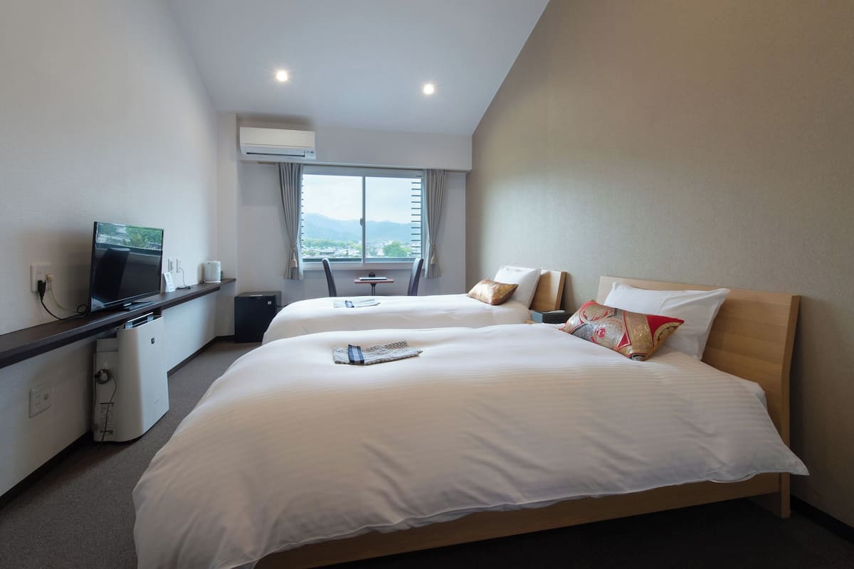 A hotel room with two beds, a desk with a television, and a window with a view of the mountains.