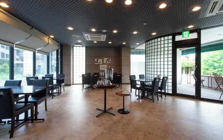 A spacious indoor area with multiple tables and chairs, large windows, and a ceiling with recessed lighting.