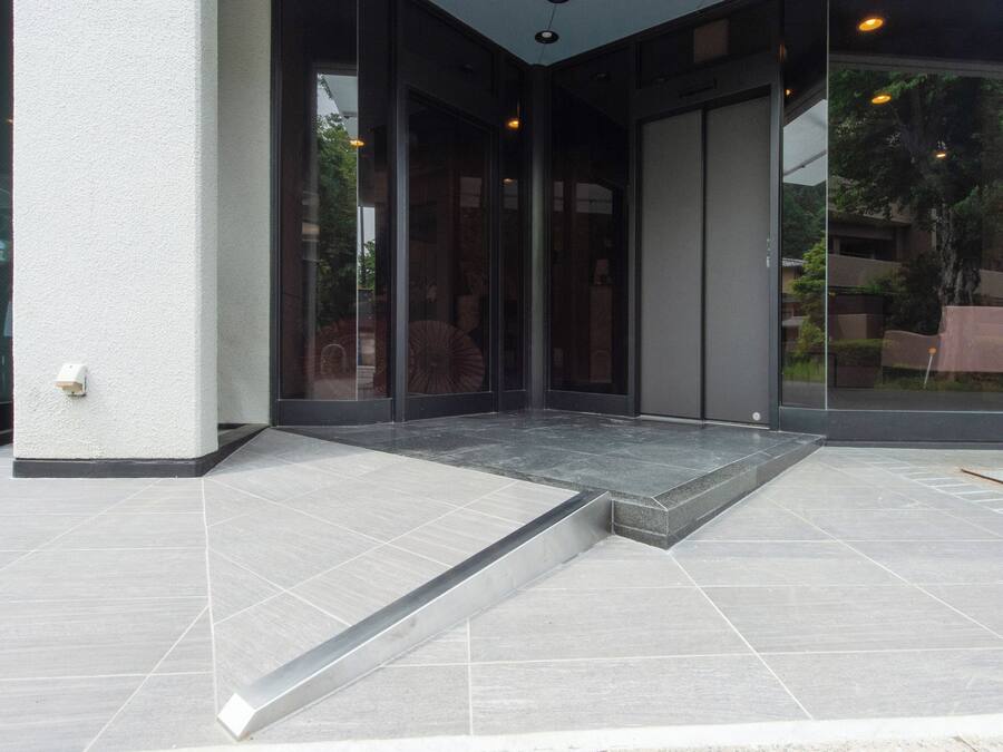 A modern building entrance with a glass door, a small outdoor seating area, and a tiled floor.