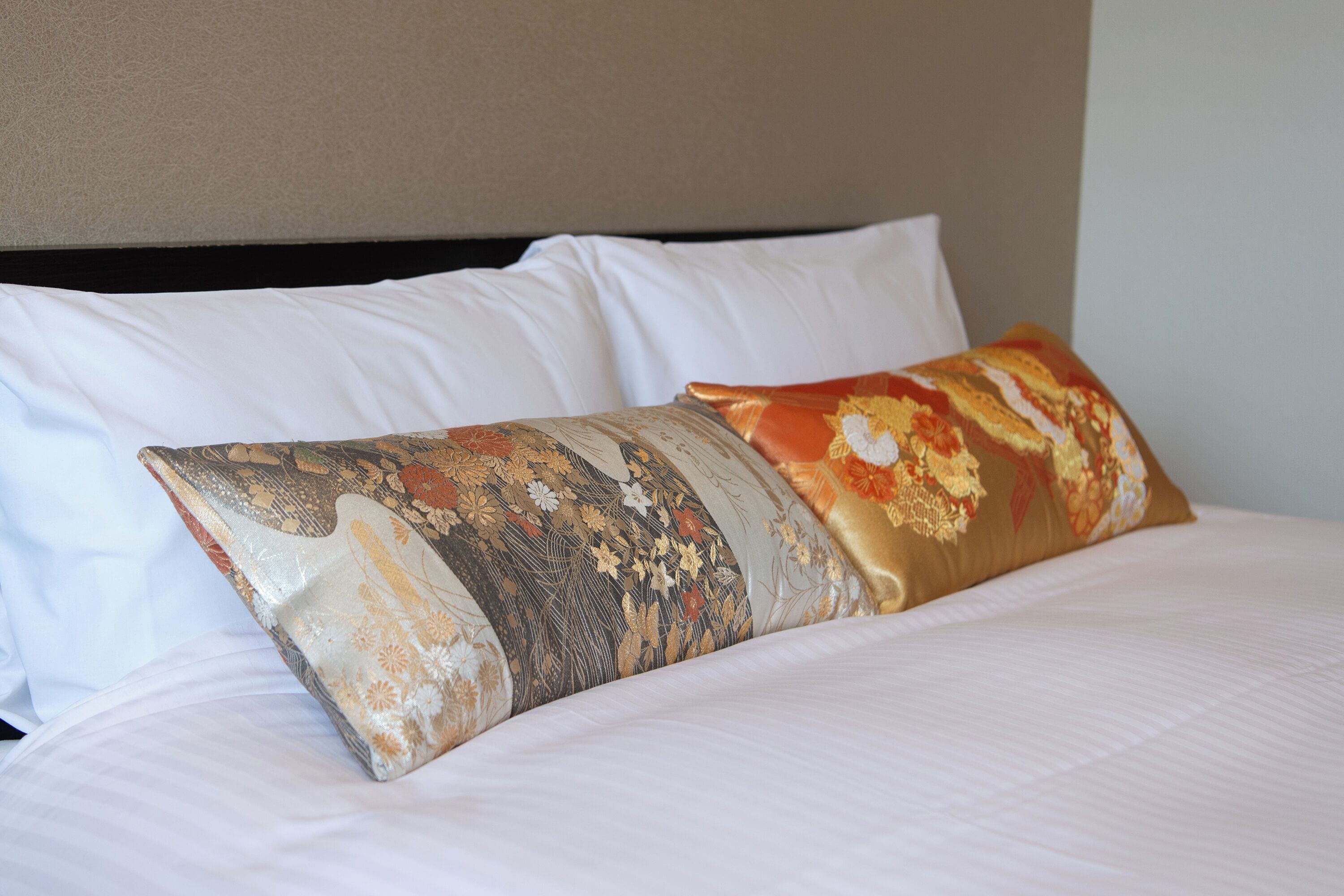 Un lit avec du linge de lit blanc et deux coussins décoratifs à motifs floraux.