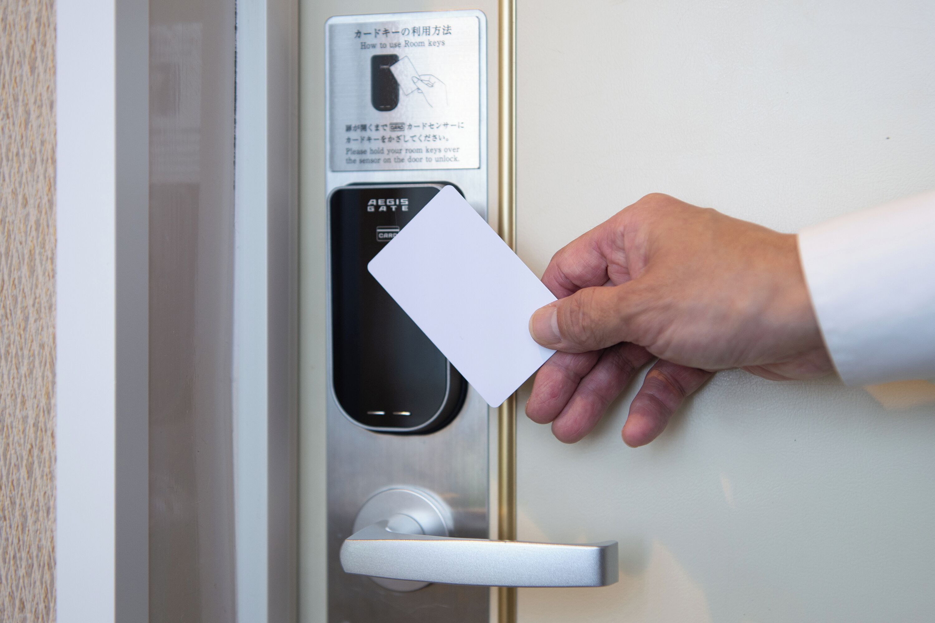 Une main tenant une carte près d’une porte équipée d’un lecteur de cartes et d’instructions rédigées dans une langue étrangère.