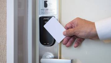 Une main tenant une carte près d’une porte équipée d’un lecteur de cartes et d’instructions rédigées dans une langue étrangère.