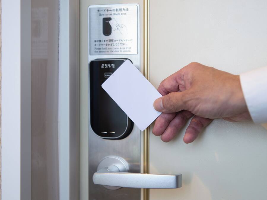 A hand holding a card near a door with a card reader and instructions in a foreign language.