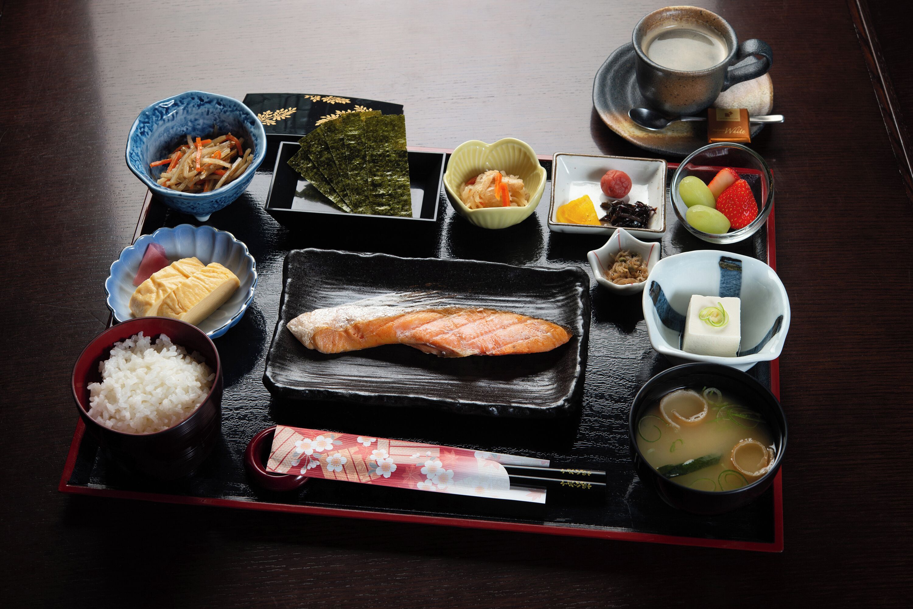 Una comida tradicional japonesa con diversos platos que incluyen arroz, pescado y sopa, servida sobre una bandeja negra.