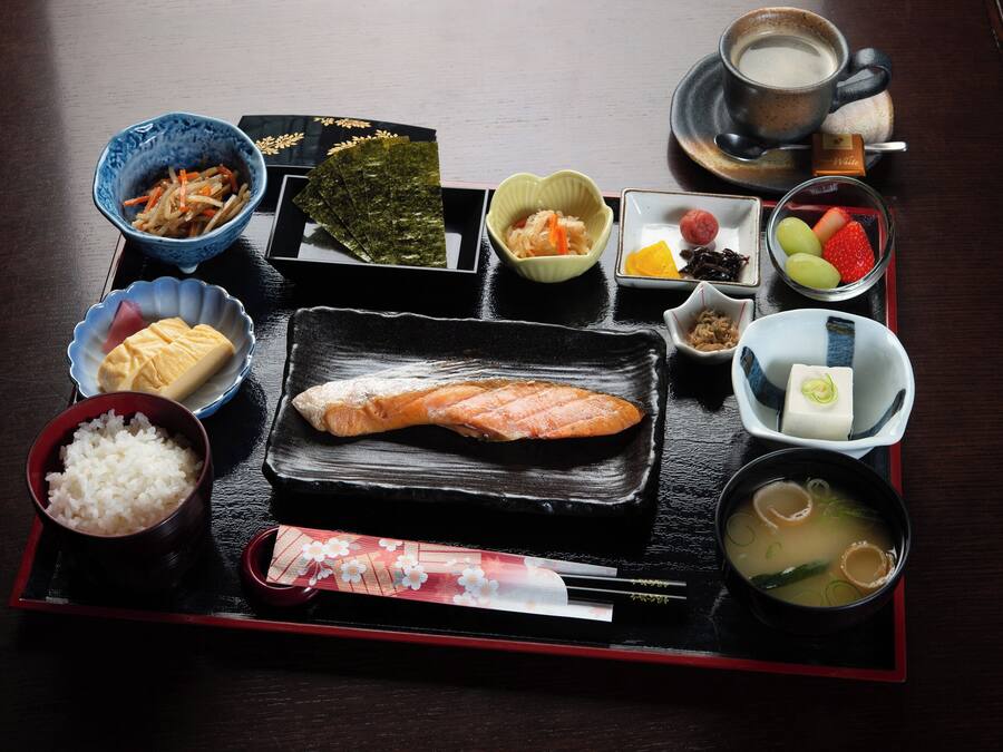A traditional Japanese meal with various dishes including rice, fish, and soup, served on a black tray.
