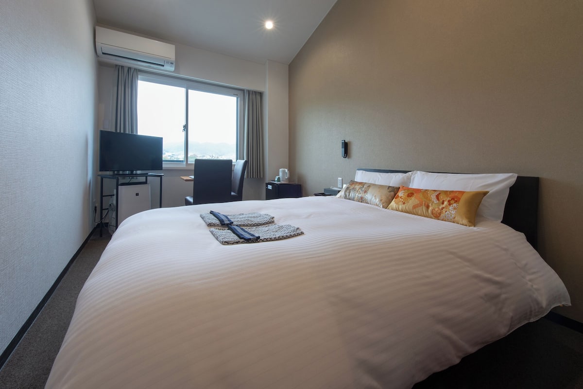 A hotel room with a large bed, a desk with a television, and a window with curtains.