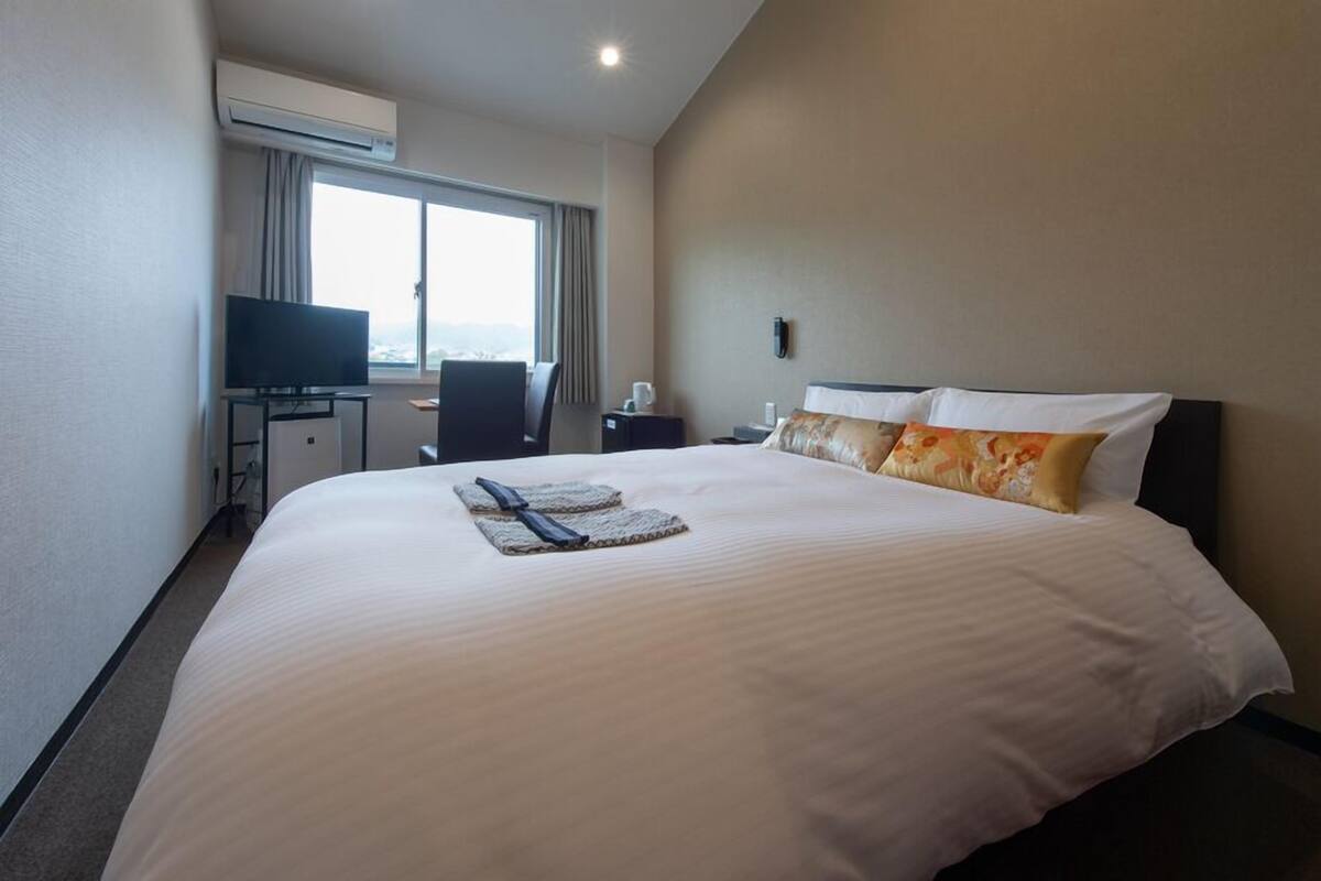 A hotel room with a large bed, a desk with a TV, and a window with curtains.