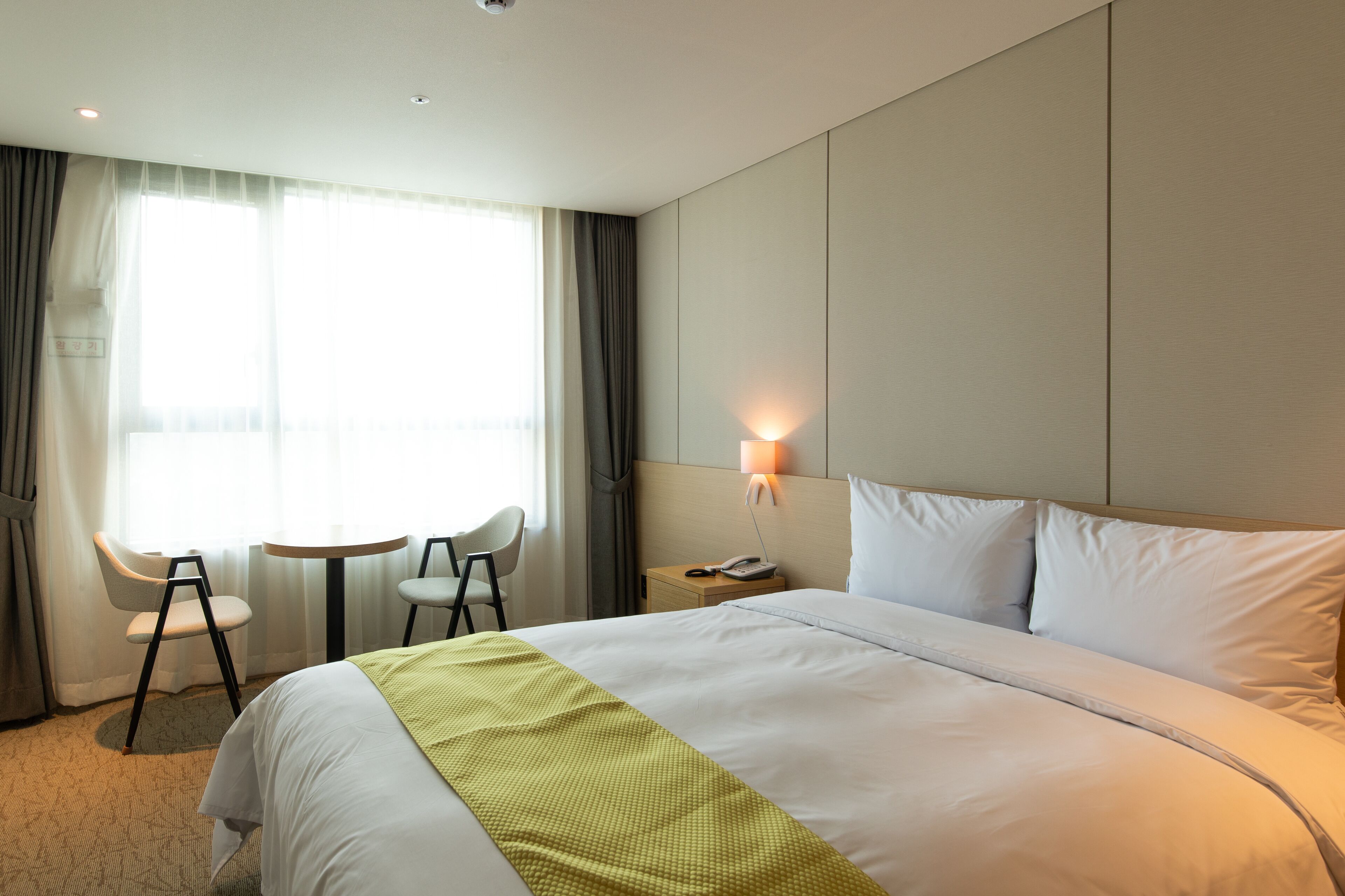 A hotel room with a large bed, two chairs, a small table, a lamp, and a window with curtains.