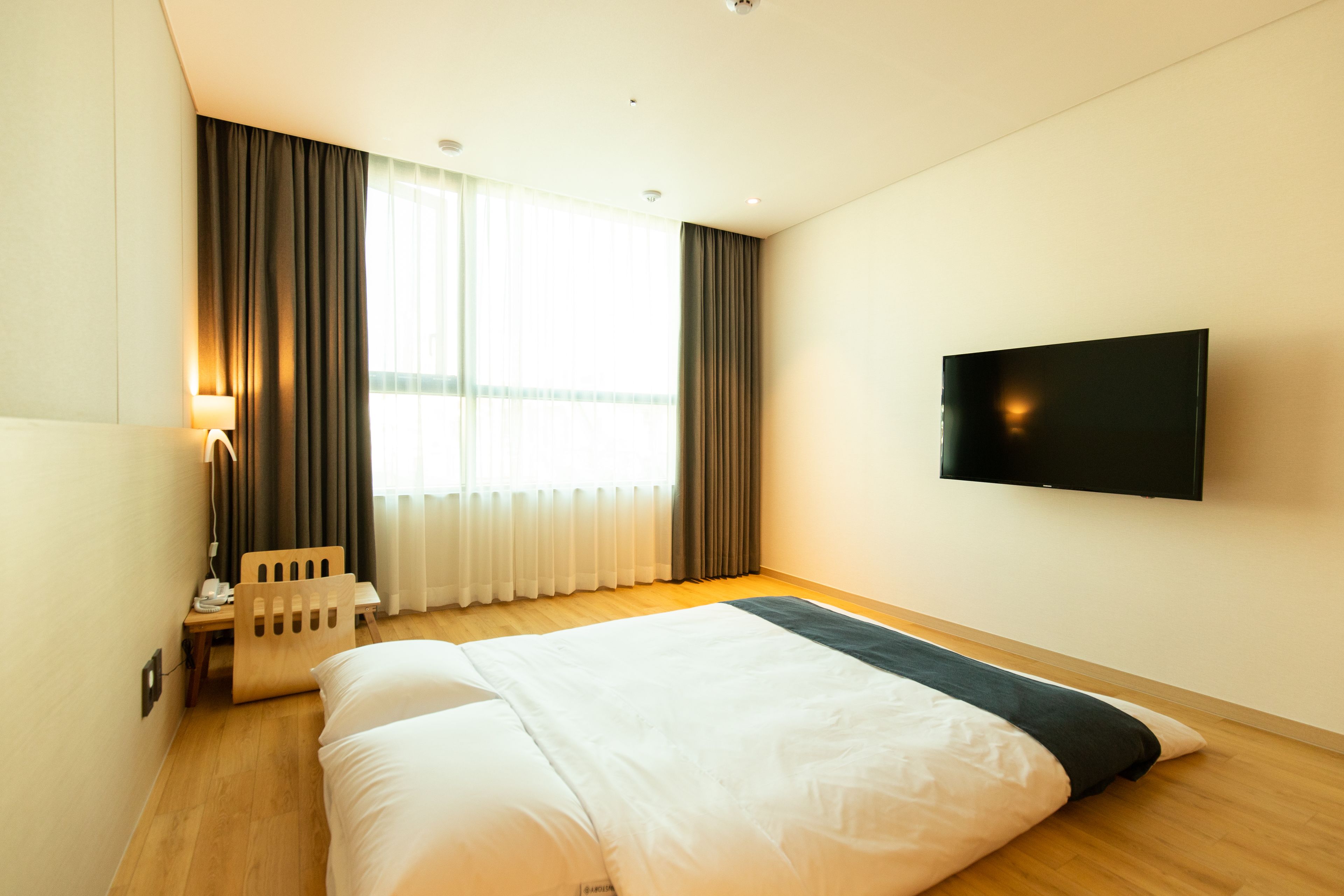 Habitació d'hotel amb un llit gran, un televisor fixat a la paret, un escriptori amb una làmpada i una finestra amb cortines.